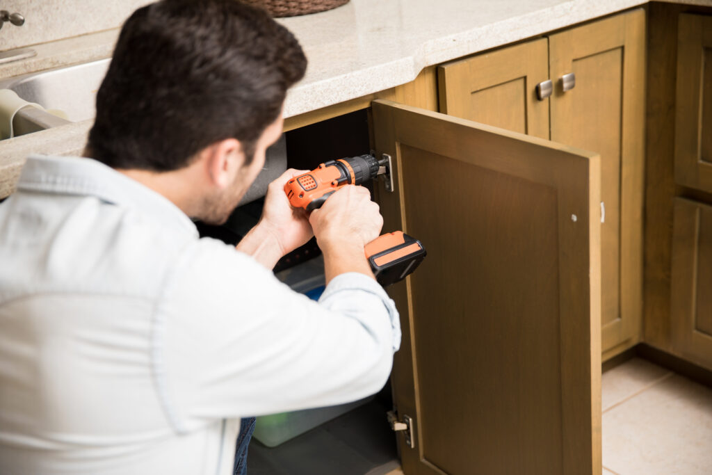 cabinet refacing vs replacement- Point of view of a young handyman using a power drill to fix a door in a kitchen cabinet