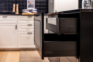 custom kitchen cabinets in 2026- Side view of a pullout drawer in a dark island with soft bokeh of white cabinets behind. Cleanliving declutter mood for modern home decor and interior styling. 